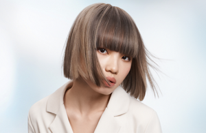 Woman with dark wavy hair wearing a white blouse in front of bright background